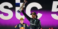 HAMILTON levanta el trofeo, y Verstappen asiste al momento sin mirarlo, y menos festejar.